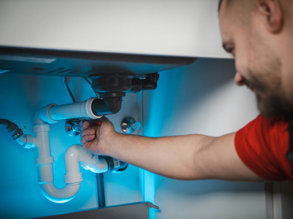 Plumber working on pipes under a sink